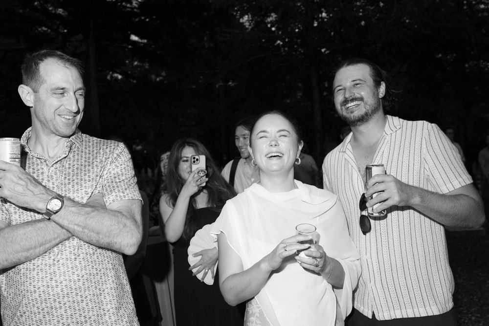 Three friends laughing together at an outdoor party, holding drinks in a black and white photo.
