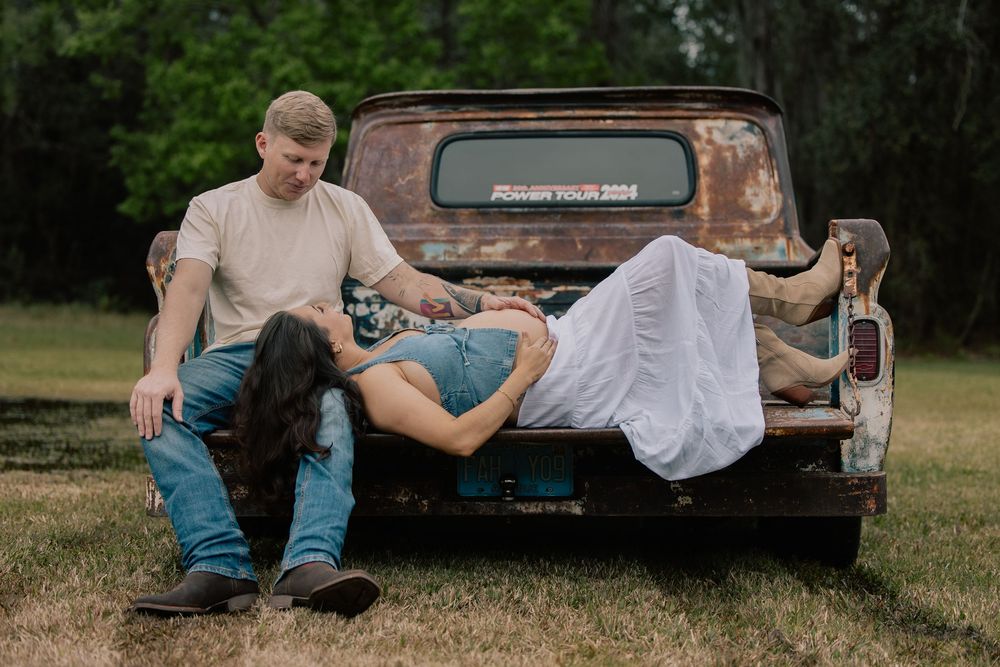 Couple relaxing on rusty vintage truck bed during outdoor maternity photo session.