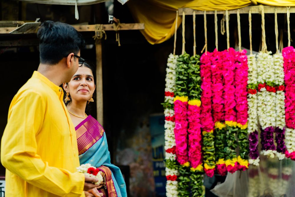 Indian couple in traditional attire browsing colorful flower garlands at a vibrant street market.