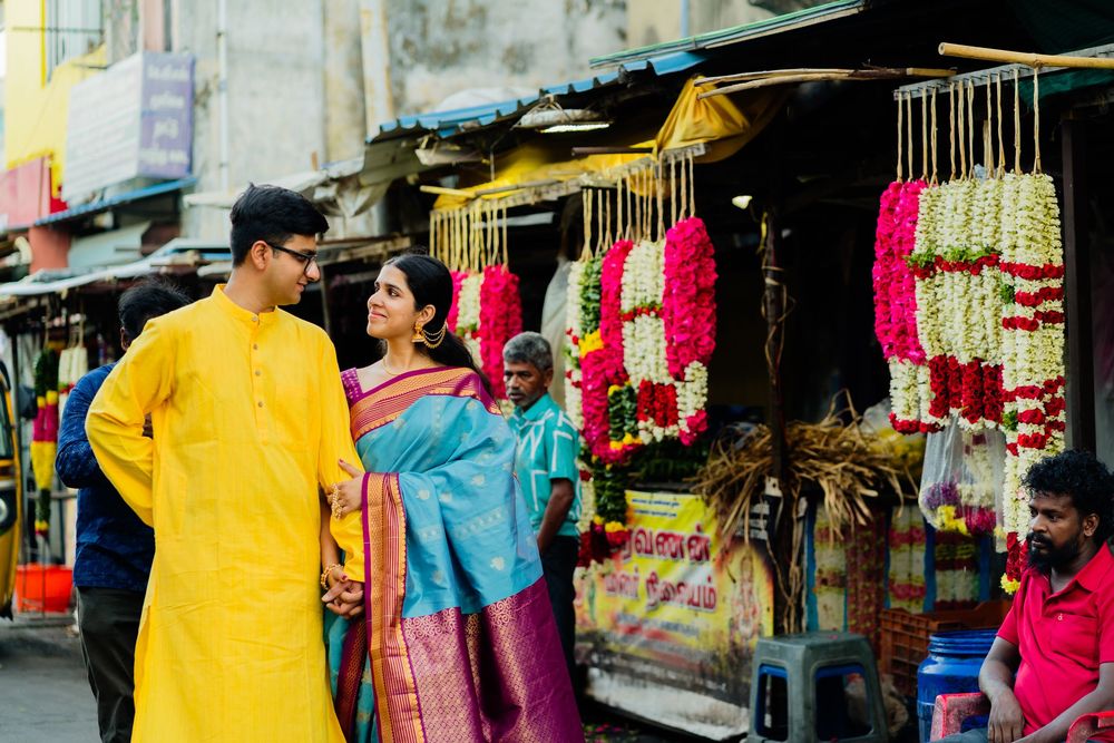 Couple in traditional Indian attire browsing colorful flower garlands at a vibrant street market stall.