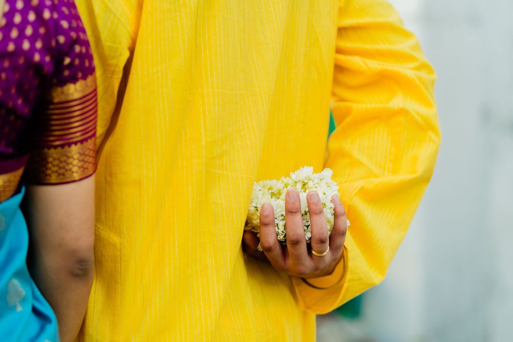 Close-up of Indian couple holding white jasmine flowers, man in yellow kurta, woman in purple saree.