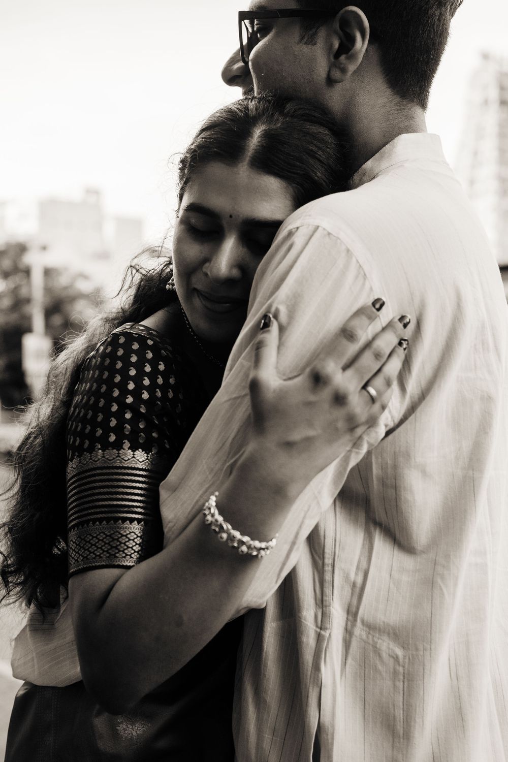 Indian couple sharing a tender embrace, woman in black saree with pearl bracelet, black and white photo.