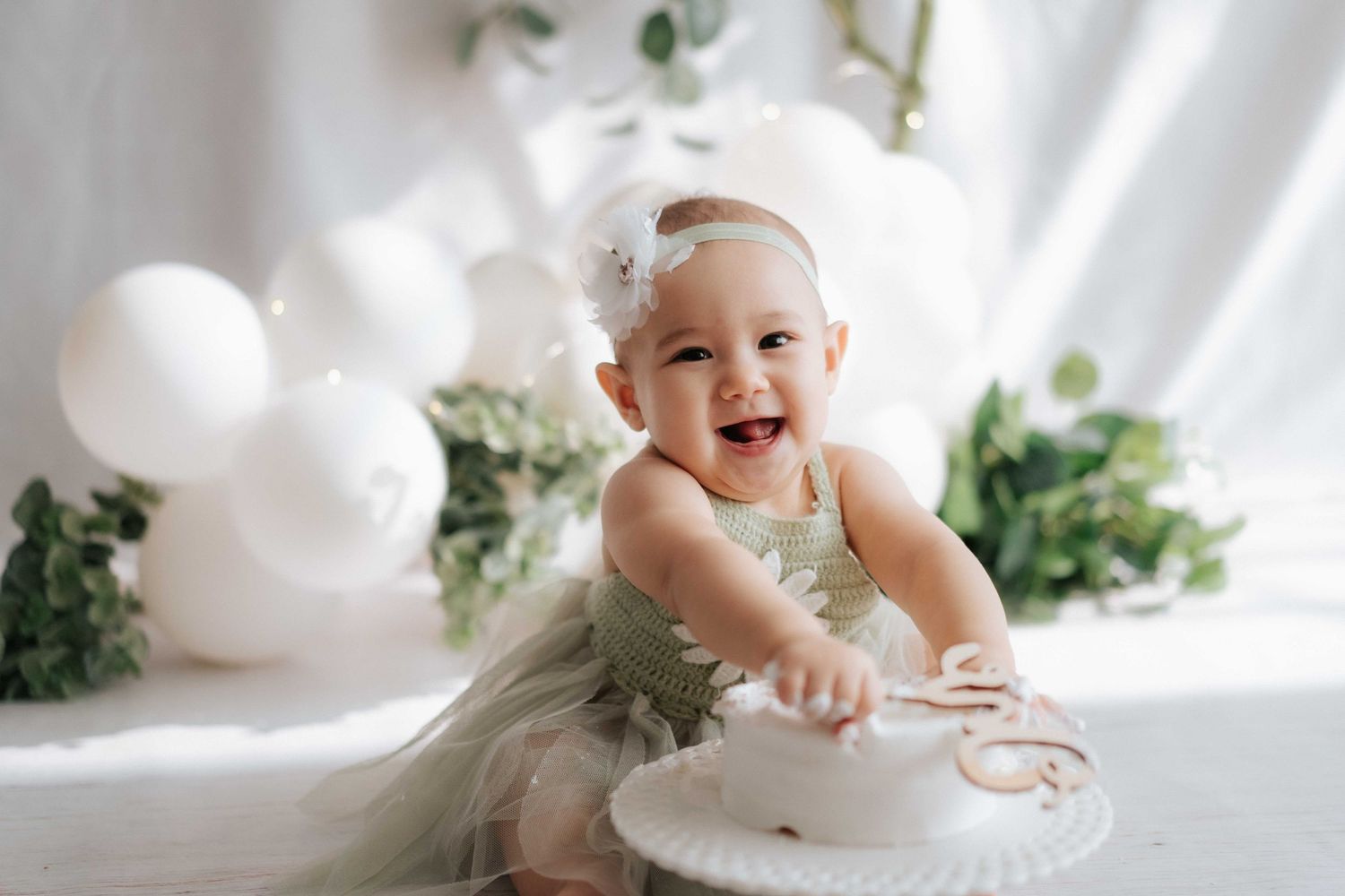 Young girl in Mardi sweatshirt and white skirt smiling, wearing green bow headband, posed near dried pampas grass.
