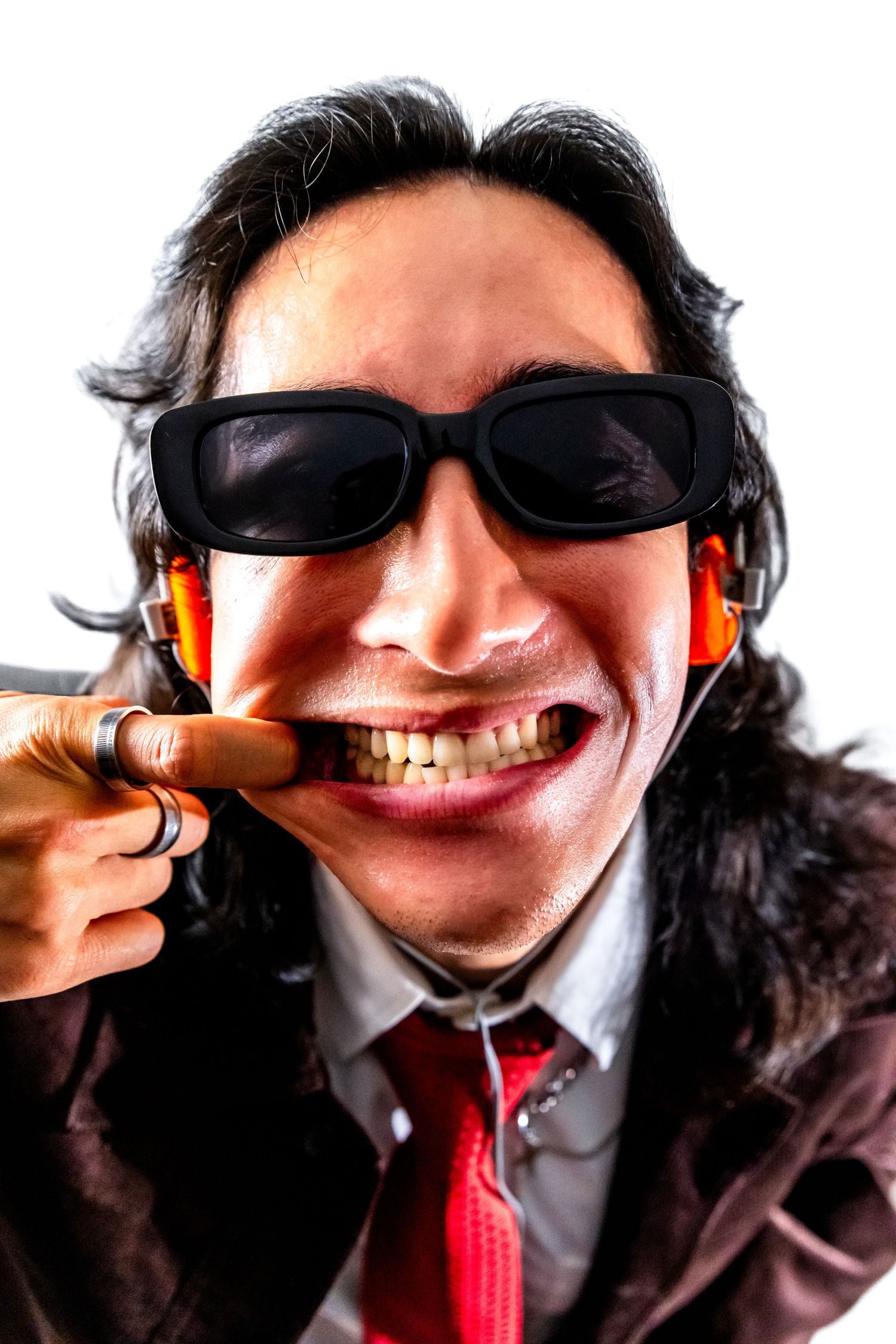 A close up portrait of Dj Can Ngyuen grabbing the inside of his mouth while wearing sunglasses and headphones with orange ear pads.
