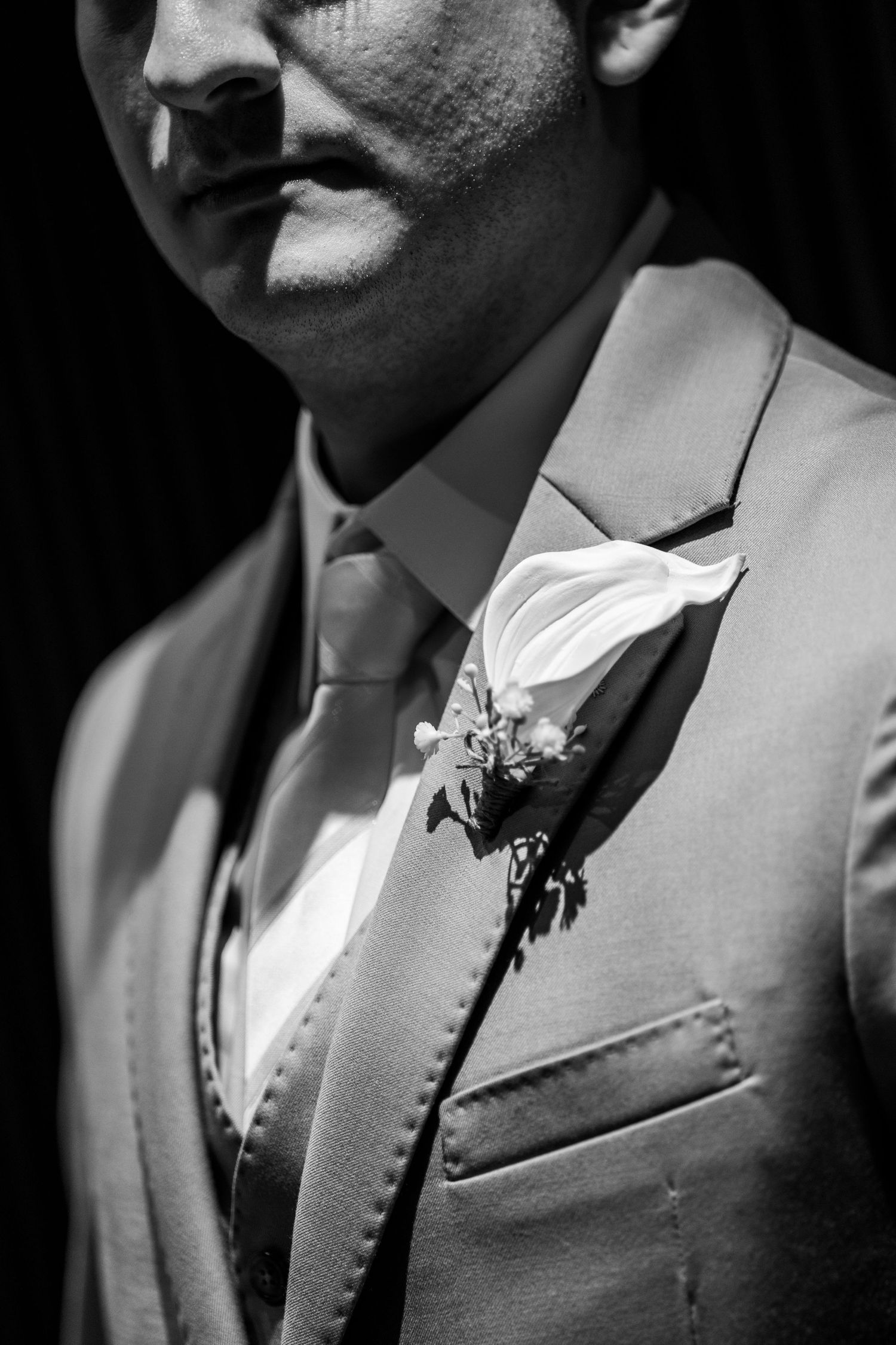 Black and white photo of a groom in a suit with a white calla lily boutonniere on his lapel.