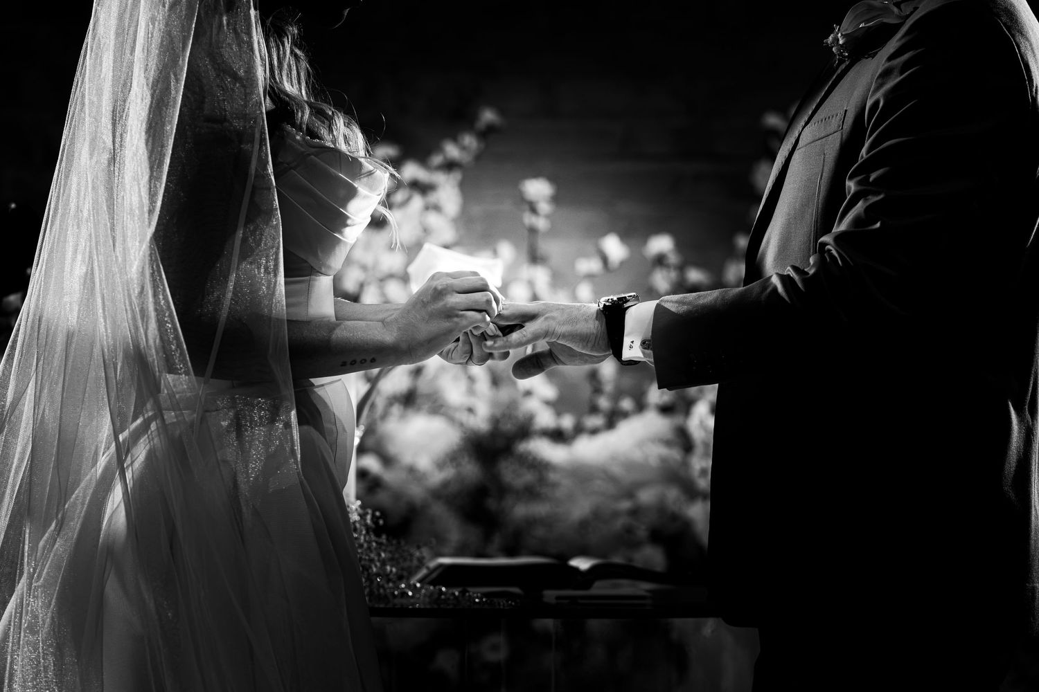 Black and white wedding ceremony photo of bride and groom exchanging rings at the altar.