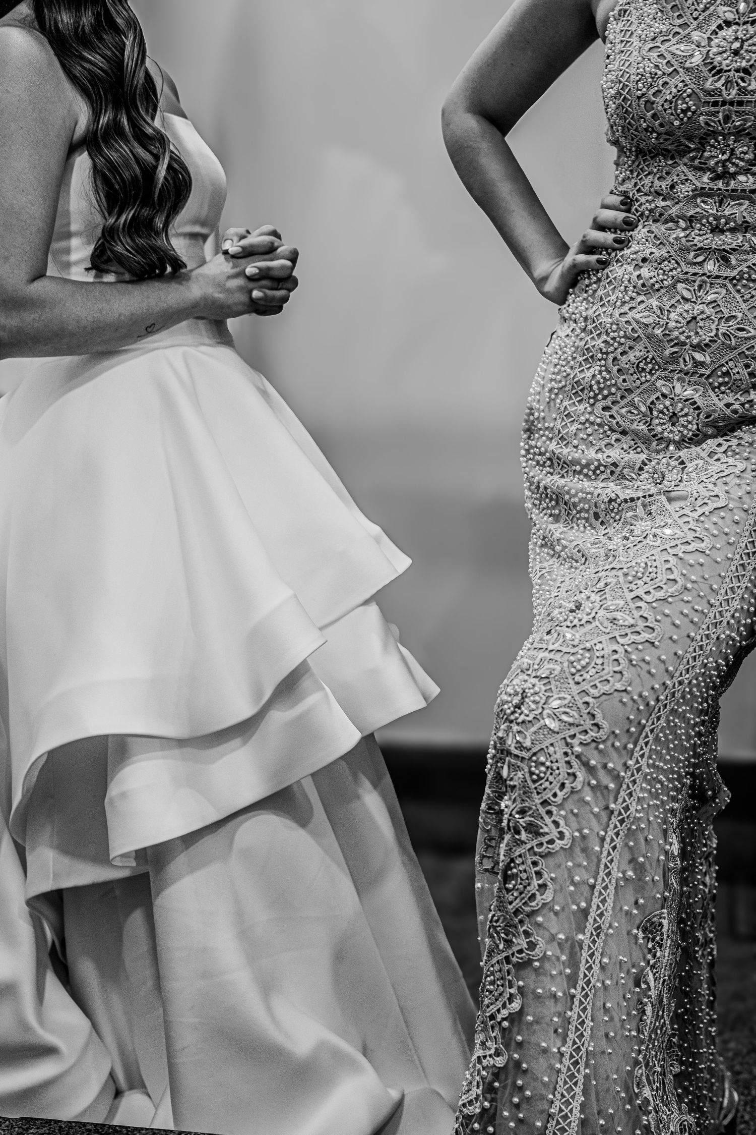 Black and white photo of bride in layered gown beside woman in beaded lace dress at wedding.