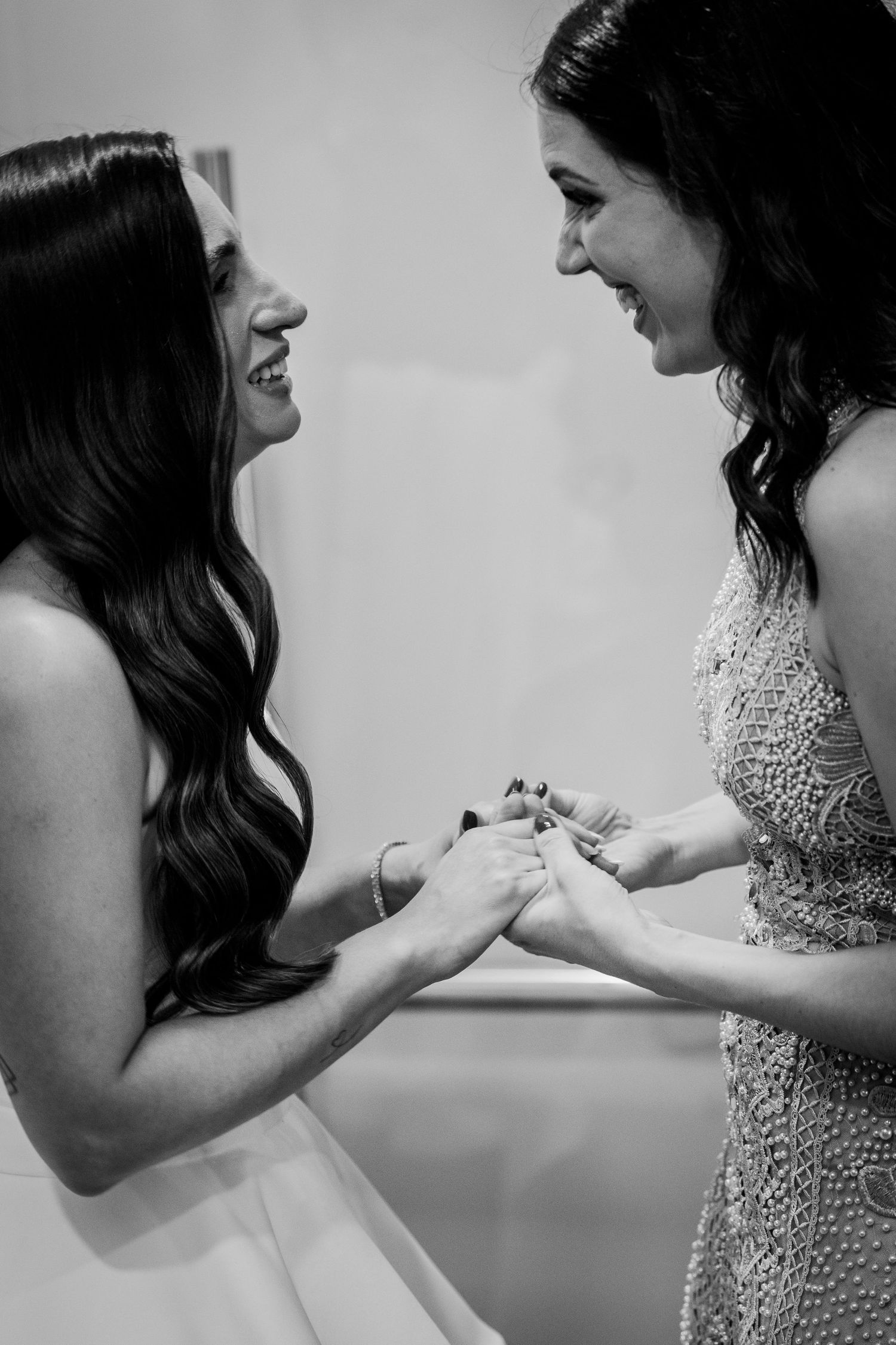 Two brides share a joyful moment exchanging rings during their wedding ceremony in black and white.