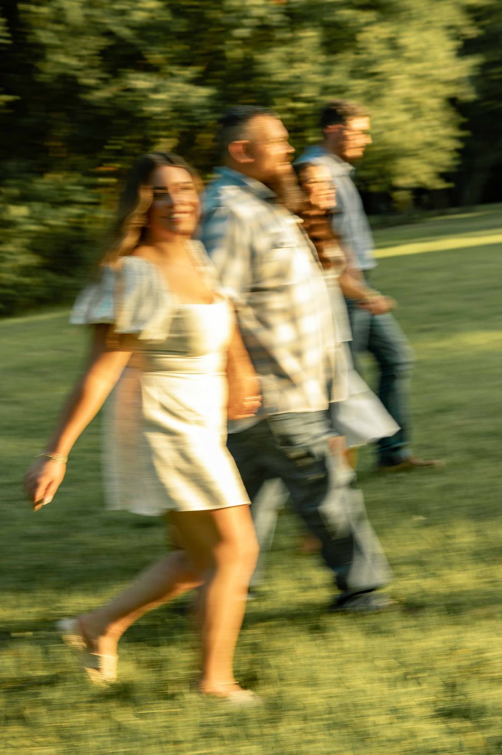 A blurred motion photo of a smiling family walking outdoors on green grass with trees in the background.