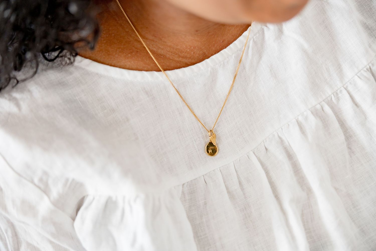 Gold teardrop pendant necklace on a woman wearing a white linen blouse.