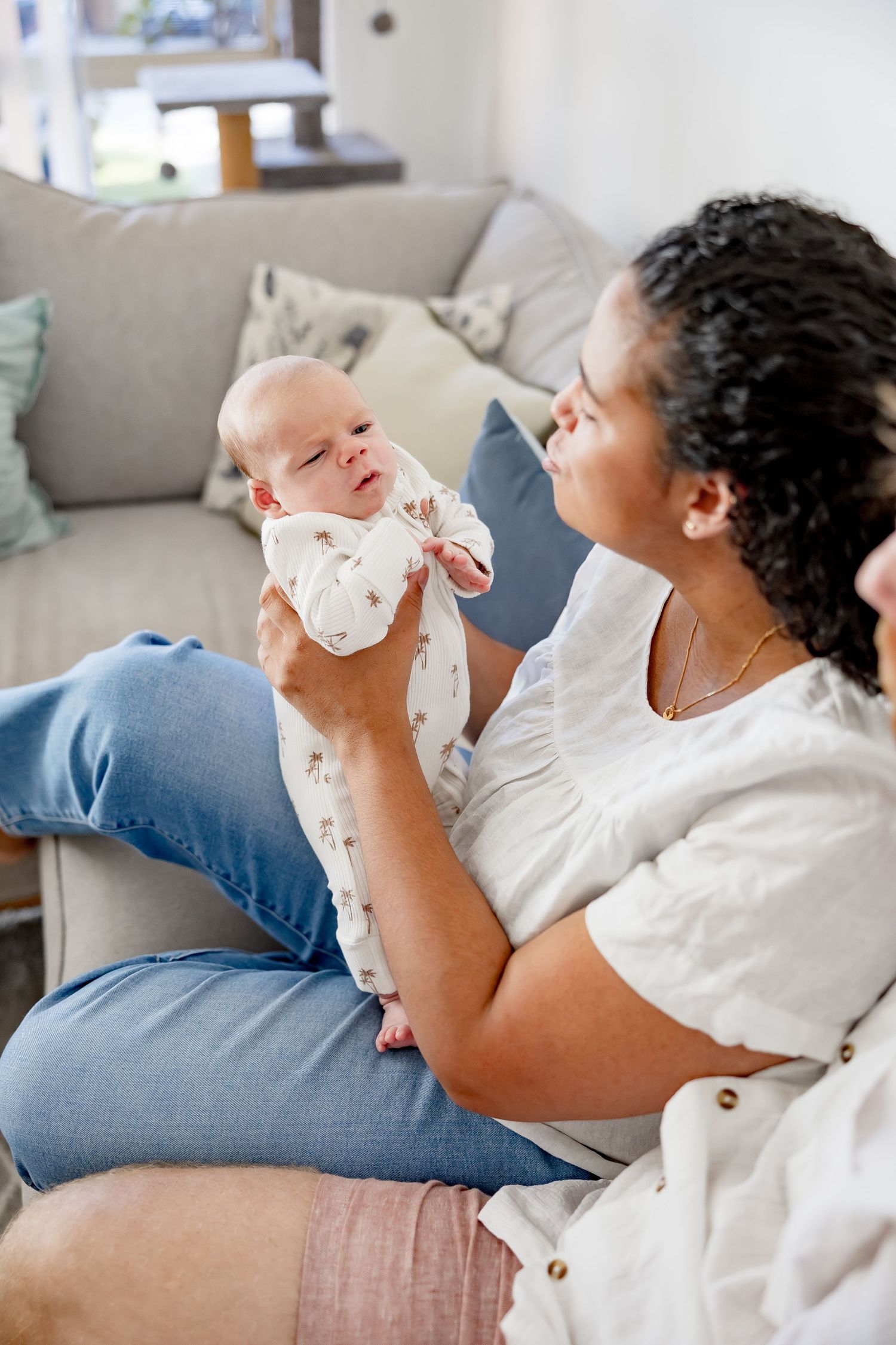 A mother holds her newborn baby up while sitting on a couch, gazing lovingly at the infant.