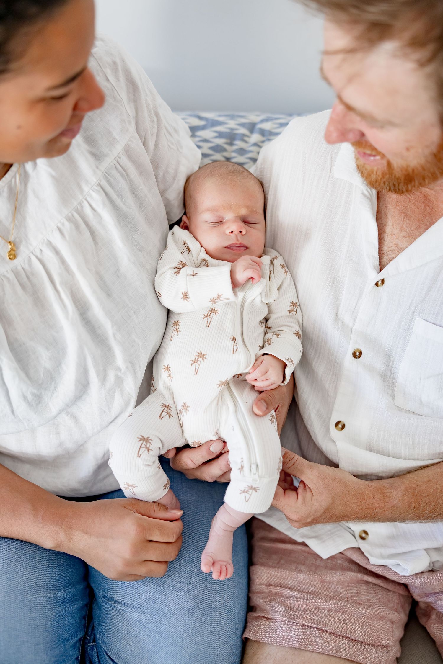 New parents admiring their sleeping newborn dressed in a floral onesie.