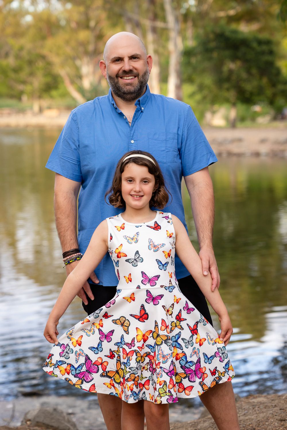 A dad poses with his daughter in front of a lake at their family photography session during golden hour