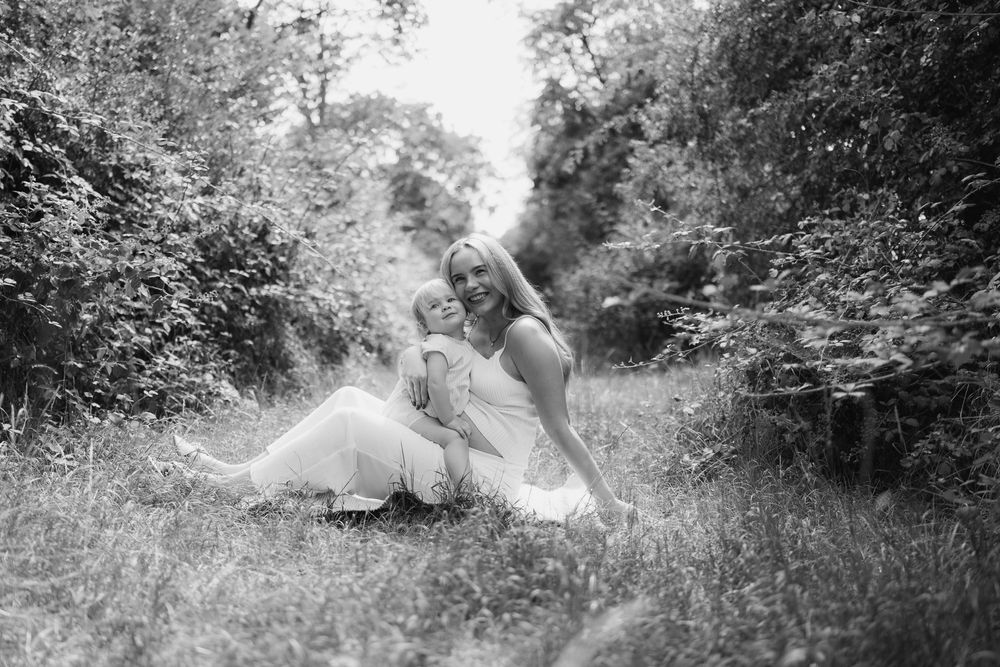 Black and white photo of a woman in a white dress sitting in a lush garden path, holding a young child.