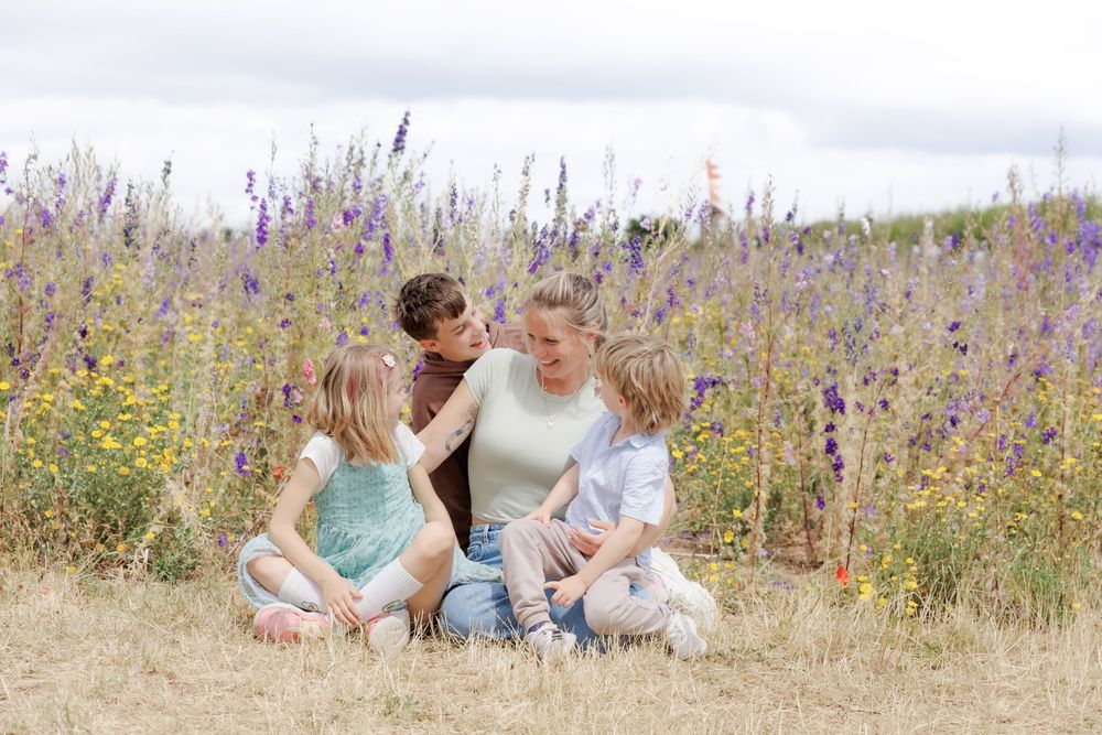 Family of four sitting together in a wildflower meadow with purple blooms, enjoying a sunny outdoor moment.