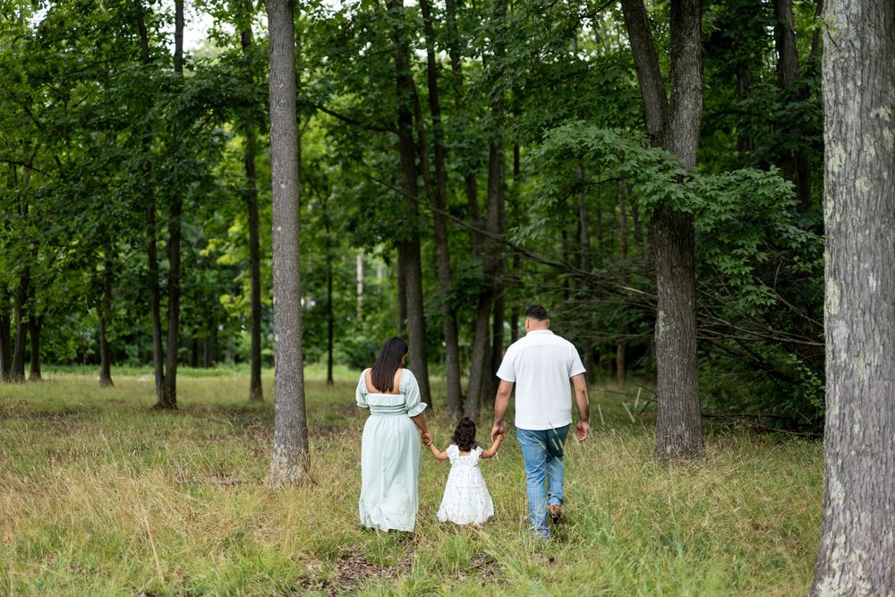 Family of three walking hand in hand through a lush green forest, parents and child enjoying a nature stroll.