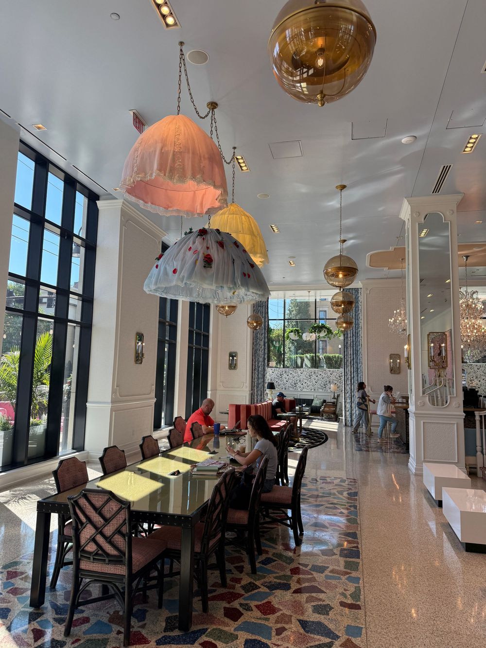 Elegant restaurant interior with colorful jellyfish pendant lights, marble floors, and tall windows flooding the space with natural light.