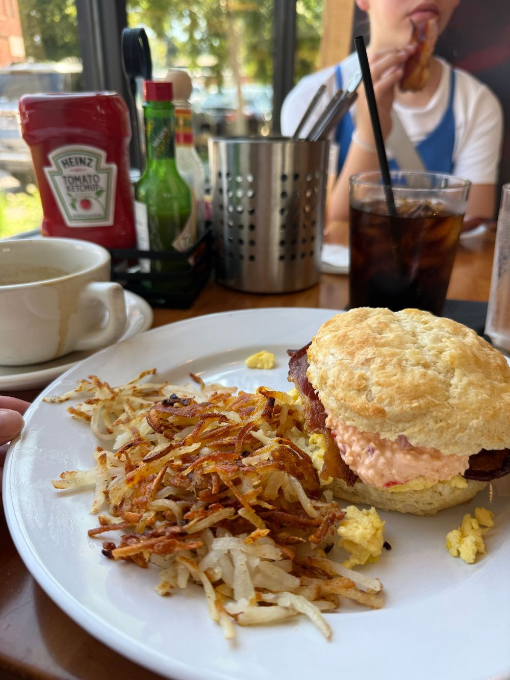 A breakfast sandwich on a biscuit with eggs and bacon served with crispy hash browns on a white plate at a diner.