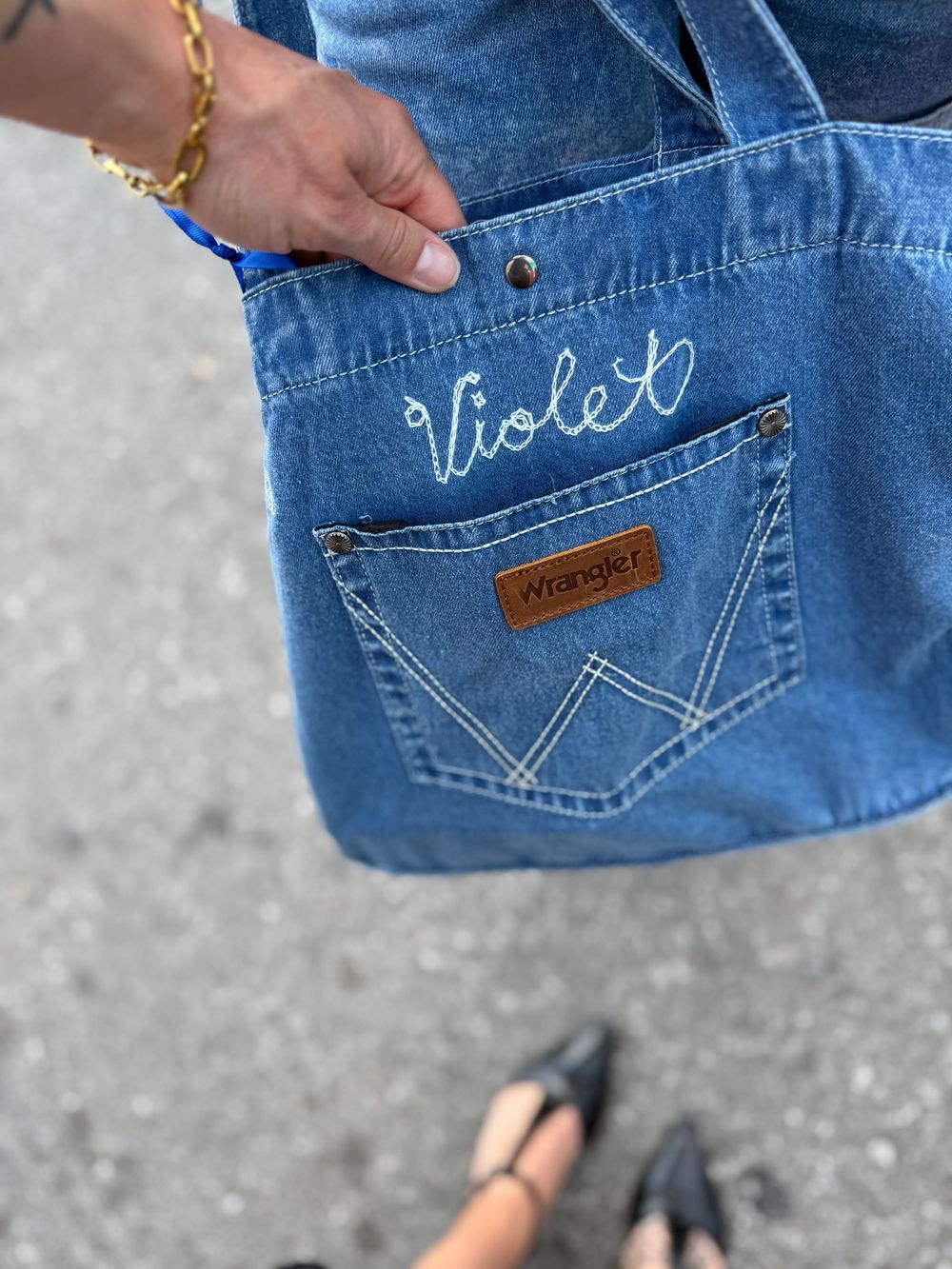 Handmade denim tote bag with embroidered name Violet and Wrangler pocket detail, held by a person outdoors.