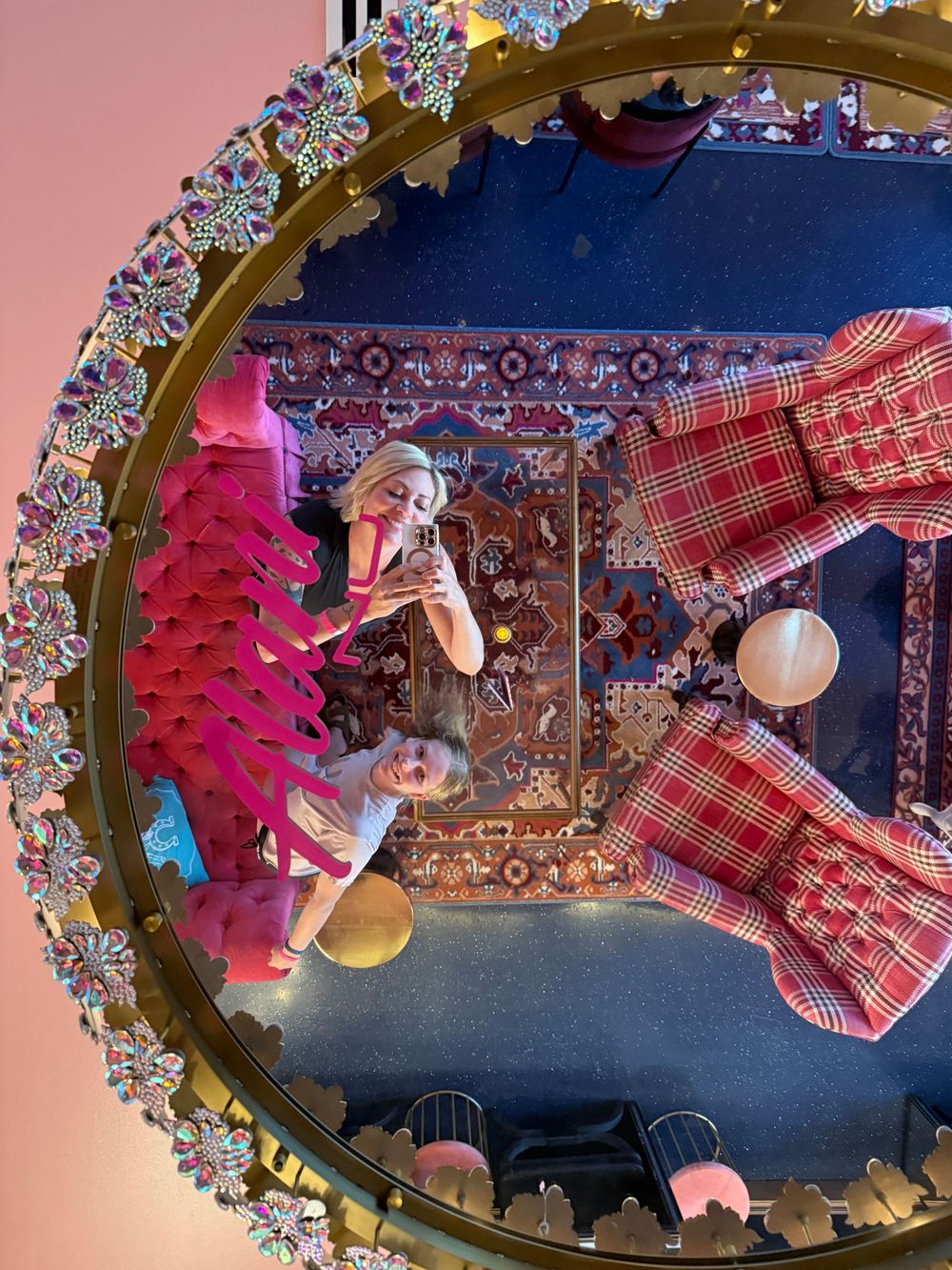 Two people taking a mirror selfie in an ornate jeweled circular mirror with colorful decor and plaid furniture.