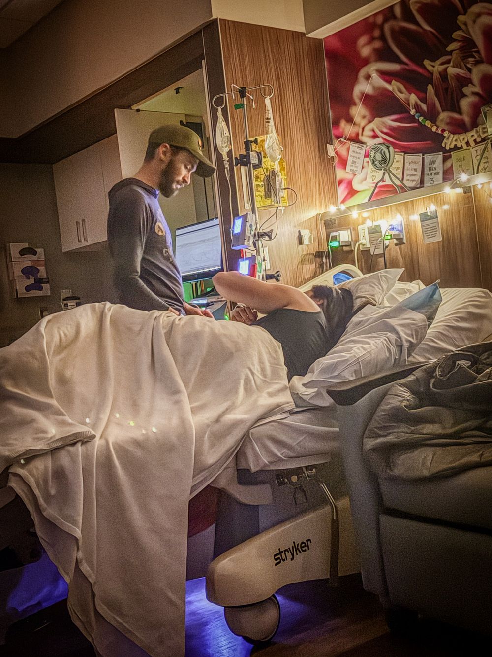 Partner supporting laboring woman in decorated hospital room at night.