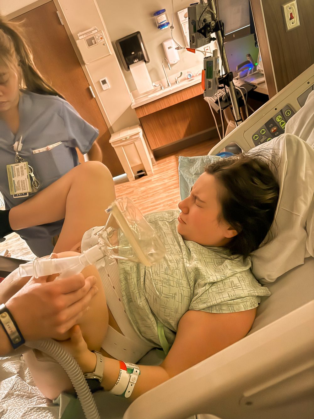 Woman in labor holding breathing tube assisted by nurse in hospital.