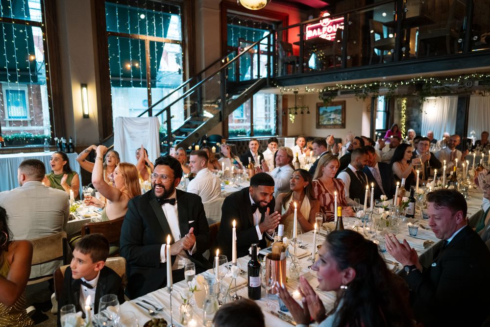 Elegant wedding reception with guests in formal attire seated at candlelit tables in a decorated venue.