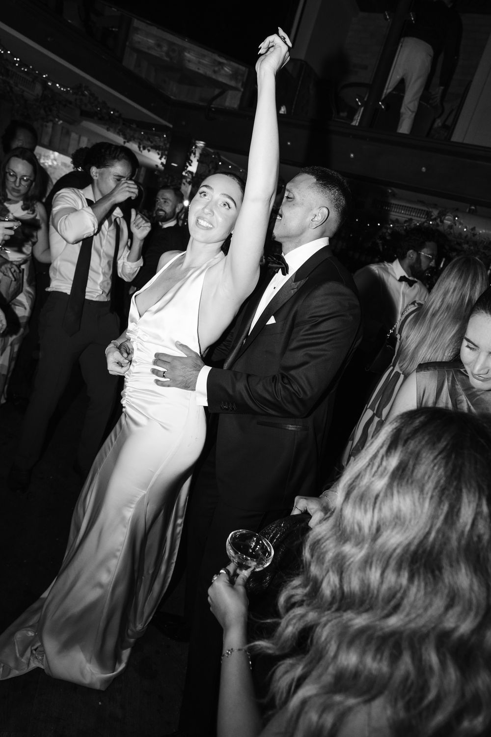 Black and white photo of a couple dancing elegantly at a formal event, woman in white gown with arm raised.