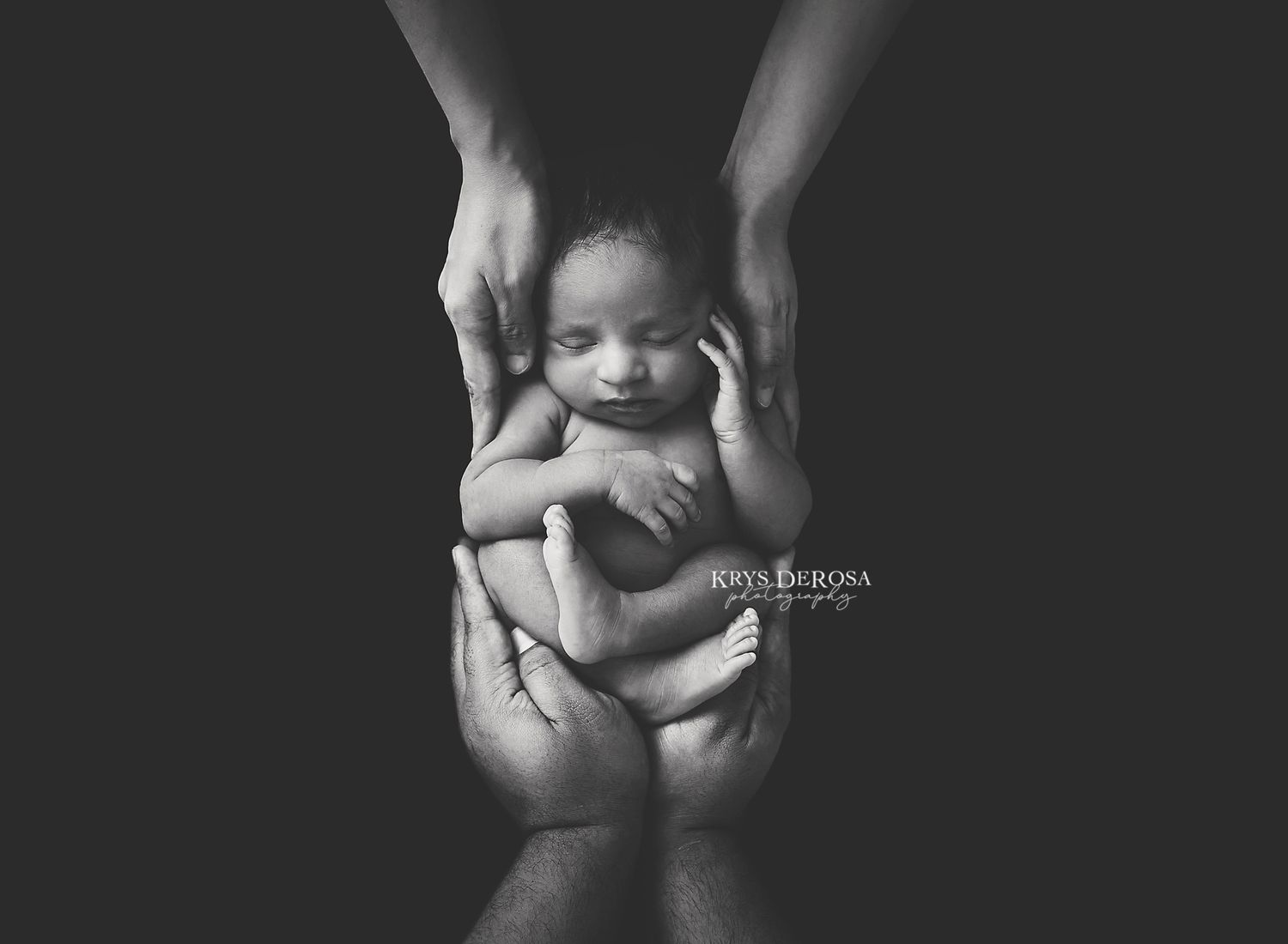 Black and white newborn photography showing tiny sleeping baby cradled in parents hands against dark background.