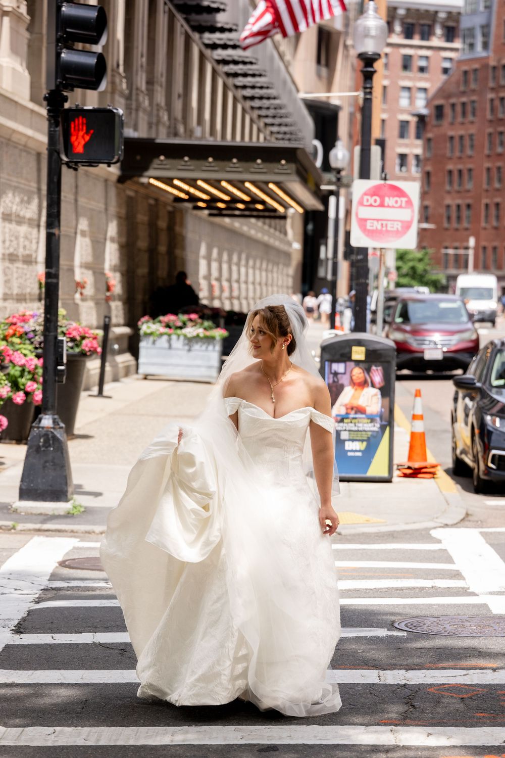 Bride in strapless white ball gown and veil crossing a city street on her wedding day.