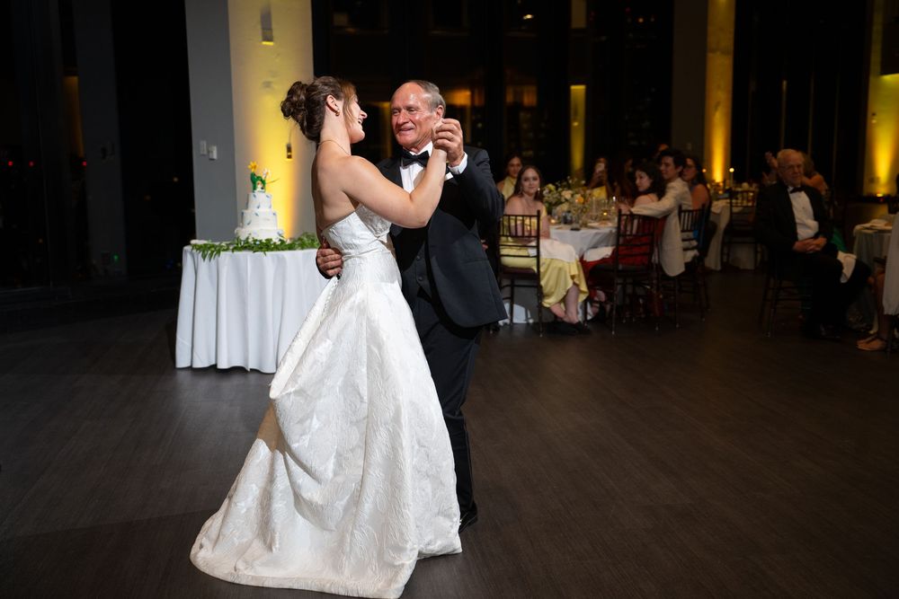 Bride and groom share their first dance at elegant wedding reception with guests seated in background.