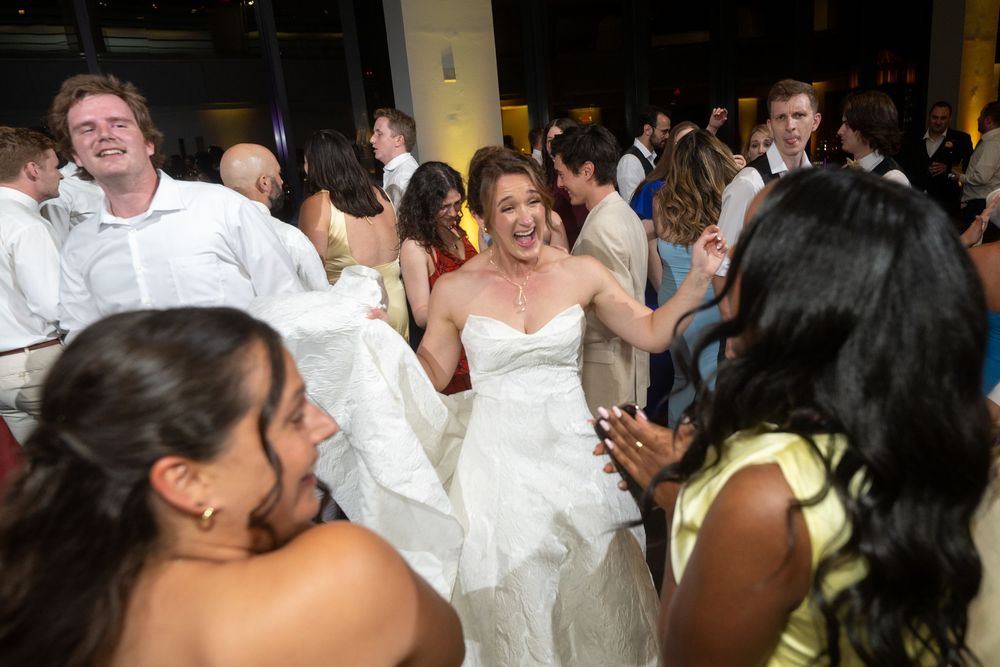 Bride in white wedding gown dancing joyfully with guests at a lively wedding reception celebration.