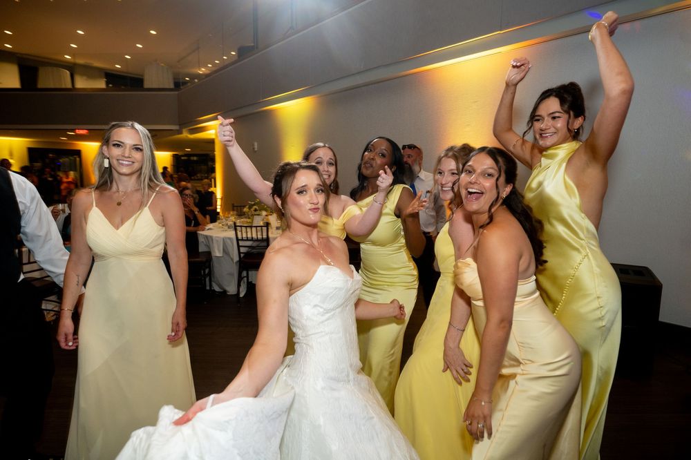 Bride in white gown celebrates with bridesmaids in yellow dresses at a festive wedding reception.