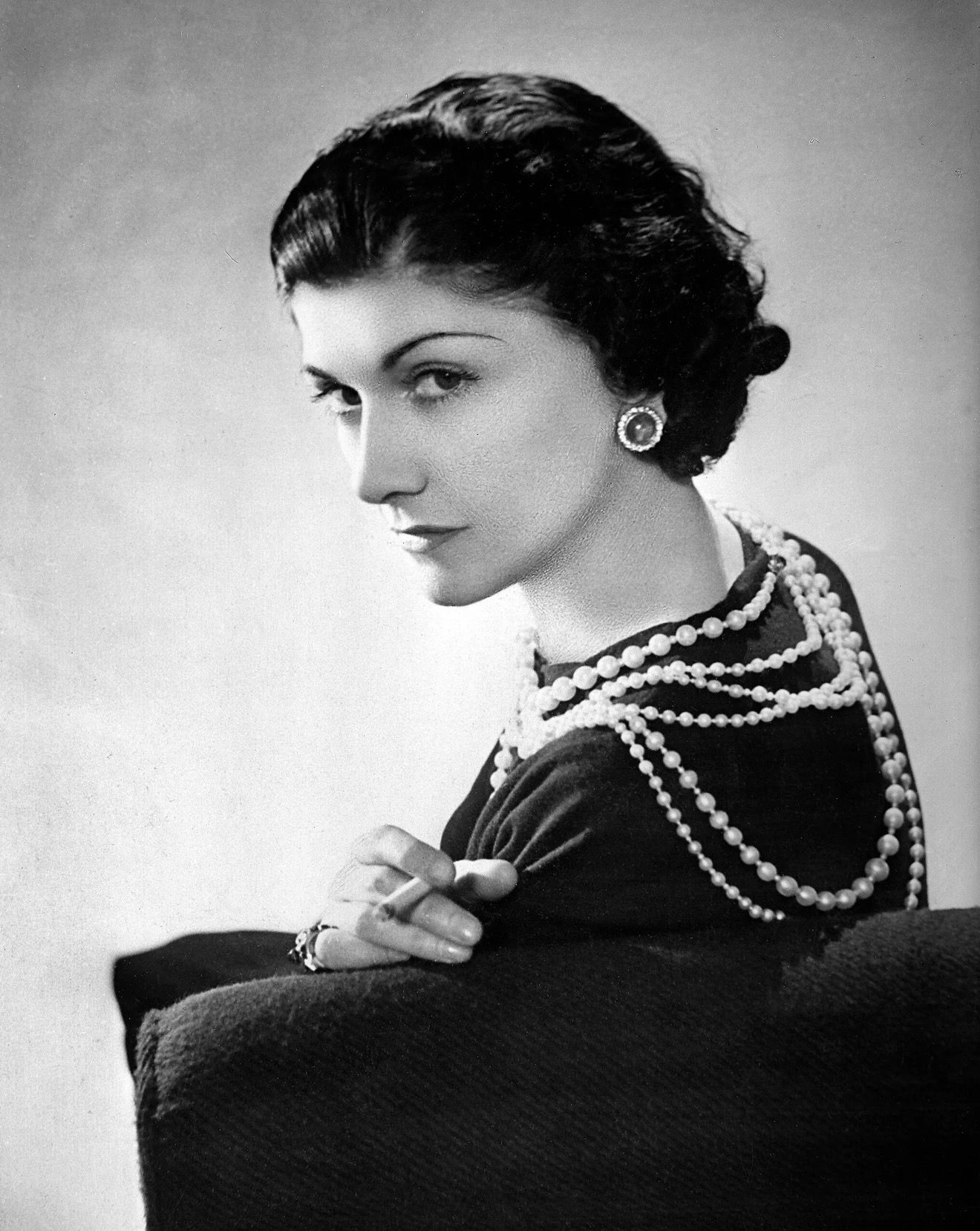 Elegant woman in black dress wearing layered pearl necklaces, vintage black and white portrait photography.