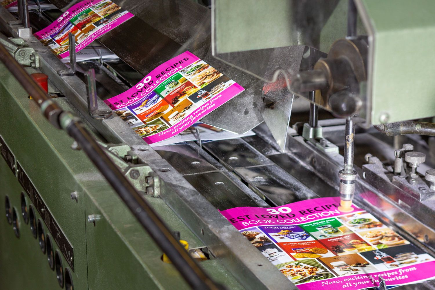 Colorful recipe booklets moving along an industrial conveyor belt in a printing facility.