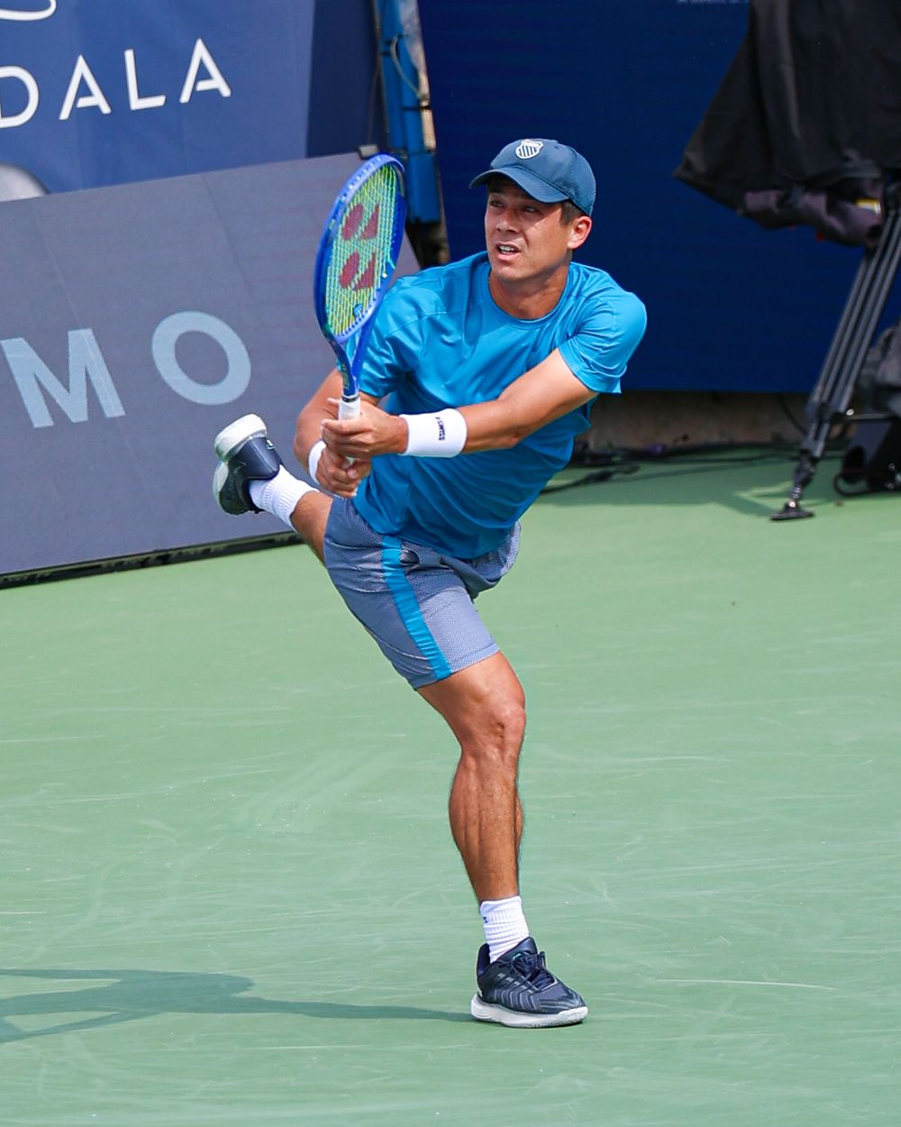 Male tennis player in blue outfit mid-swing on green court, captured in dynamic follow-through pose.