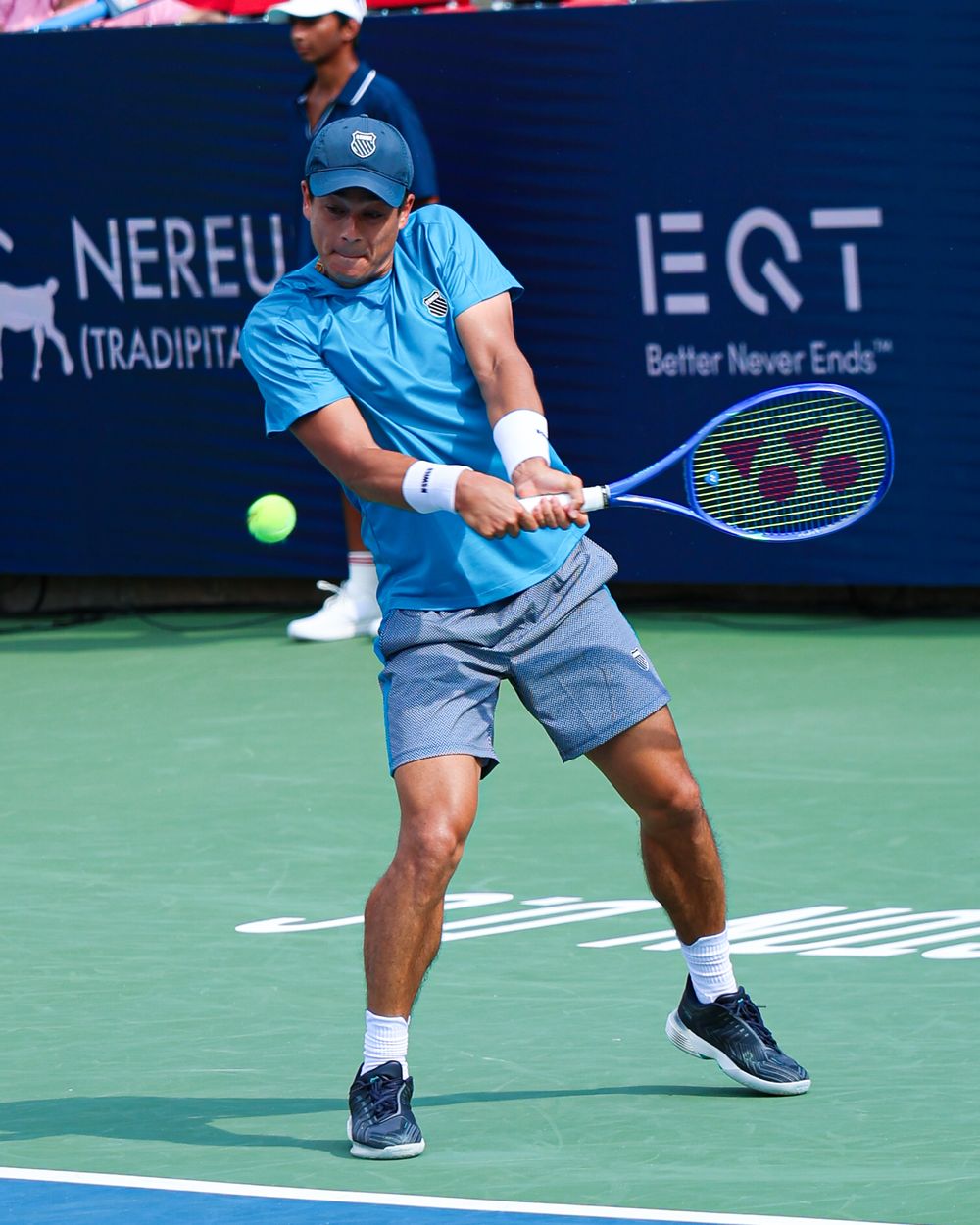 Tennis player executing a powerful two-handed backhand shot on a hard court during a professional tournament match.