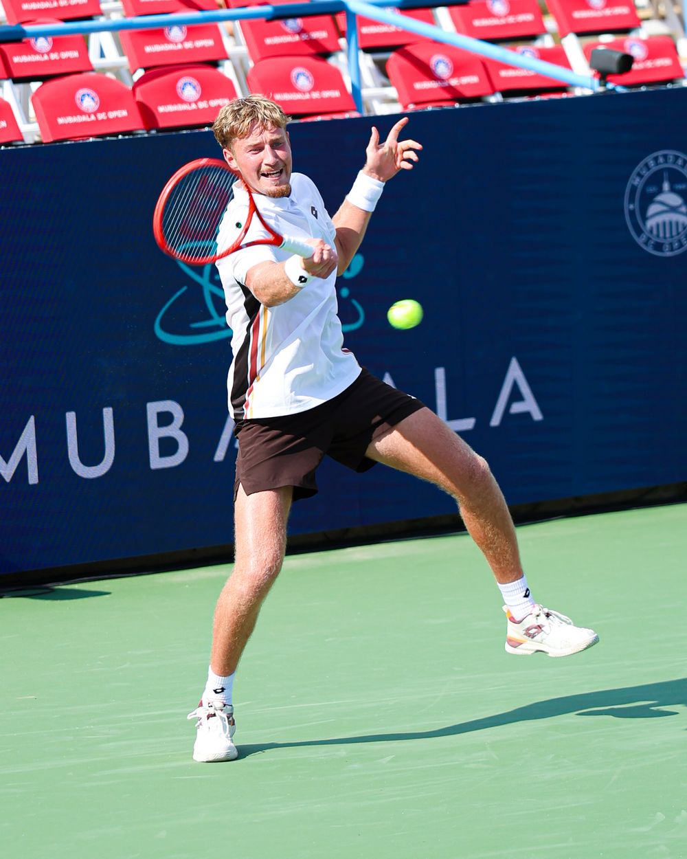 Tennis player hits a forehand shot at the Mubadala tournament on a hard court in bright sunlight.