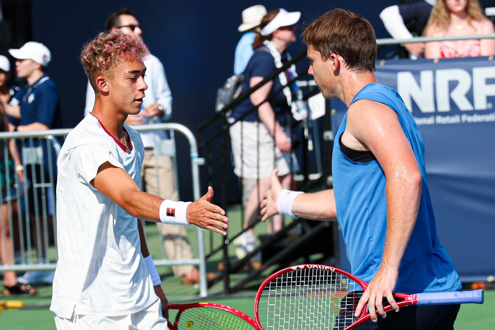 Two tennis players shaking hands at the net after a match at an outdoor tennis tournament.