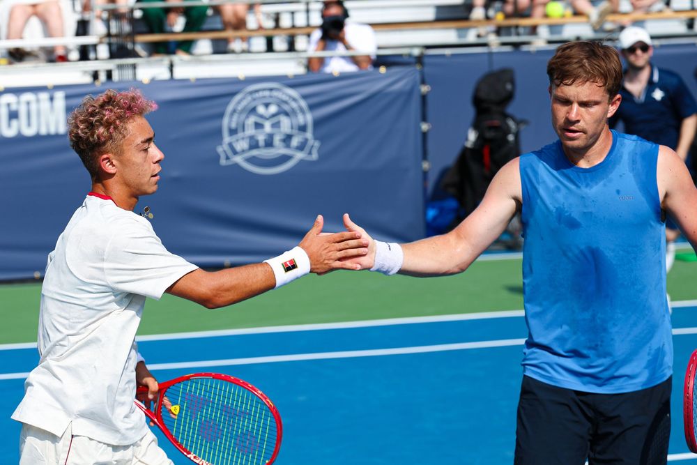 Two tennis players shaking hands over the net after a match on an outdoor hard court.