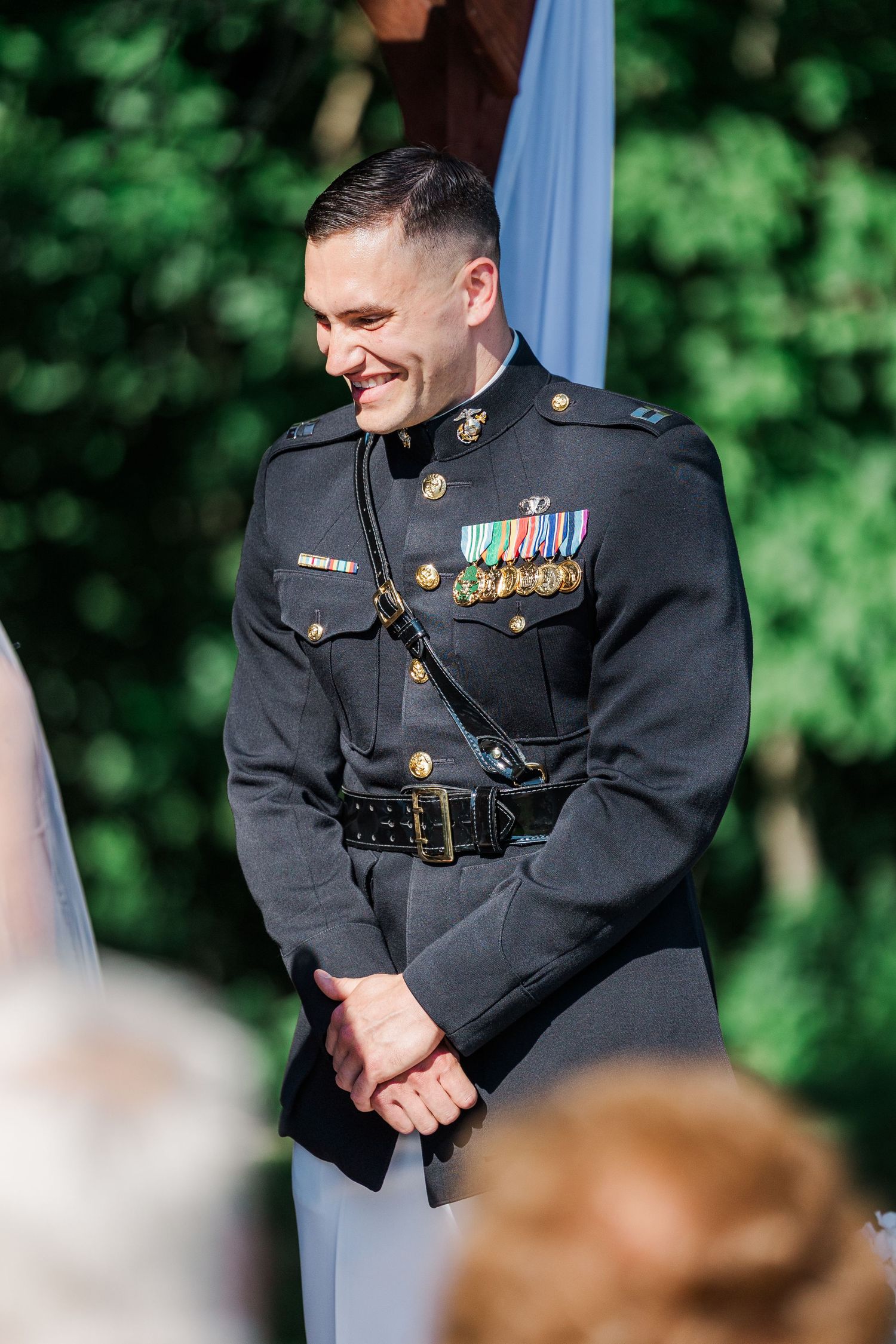 Smiling military officer in dress uniform with medals at an outdoor wedding ceremony.