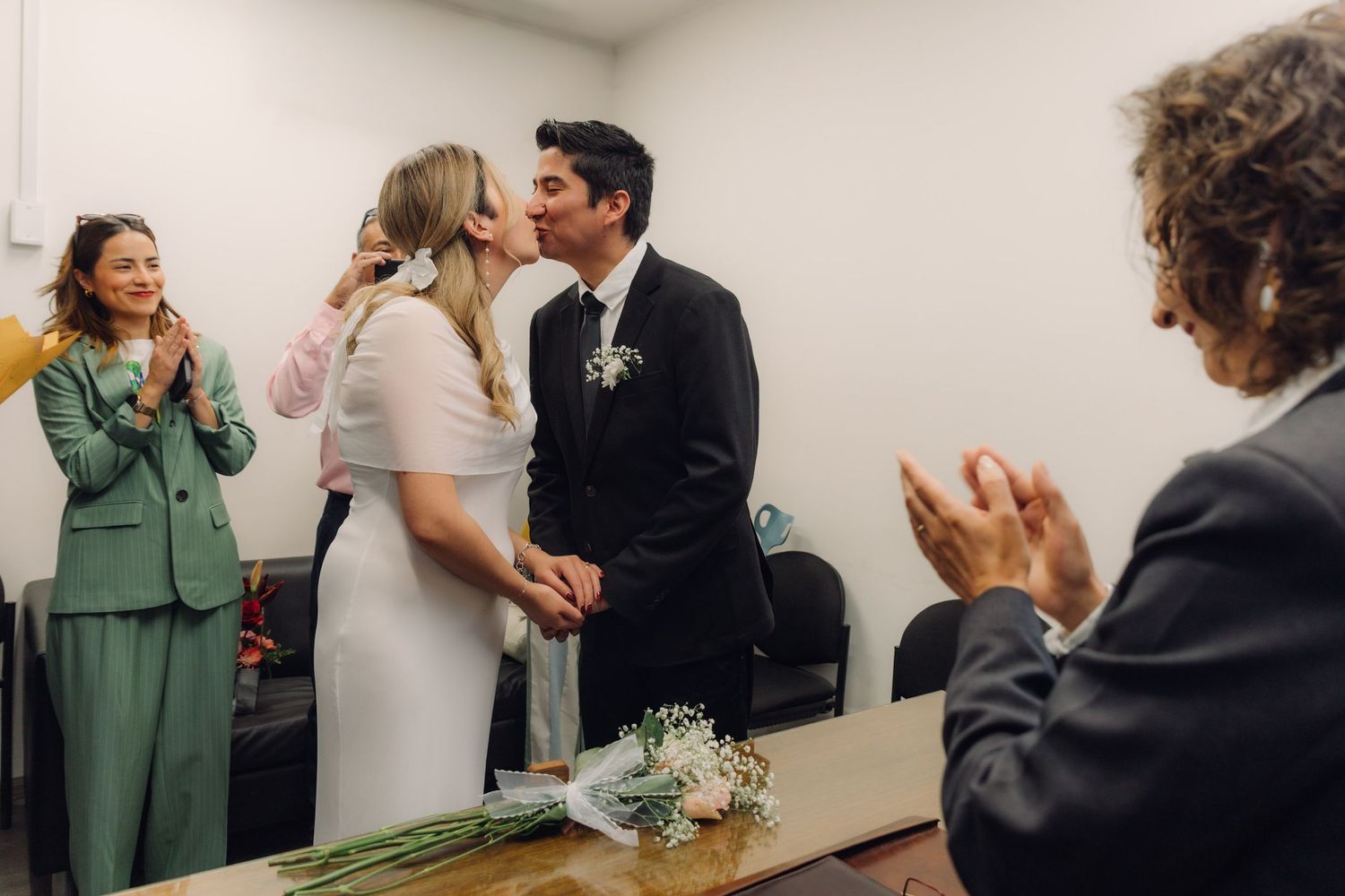 Newlywed couple sharing first kiss as married couple while guests clap during civil ceremony.
