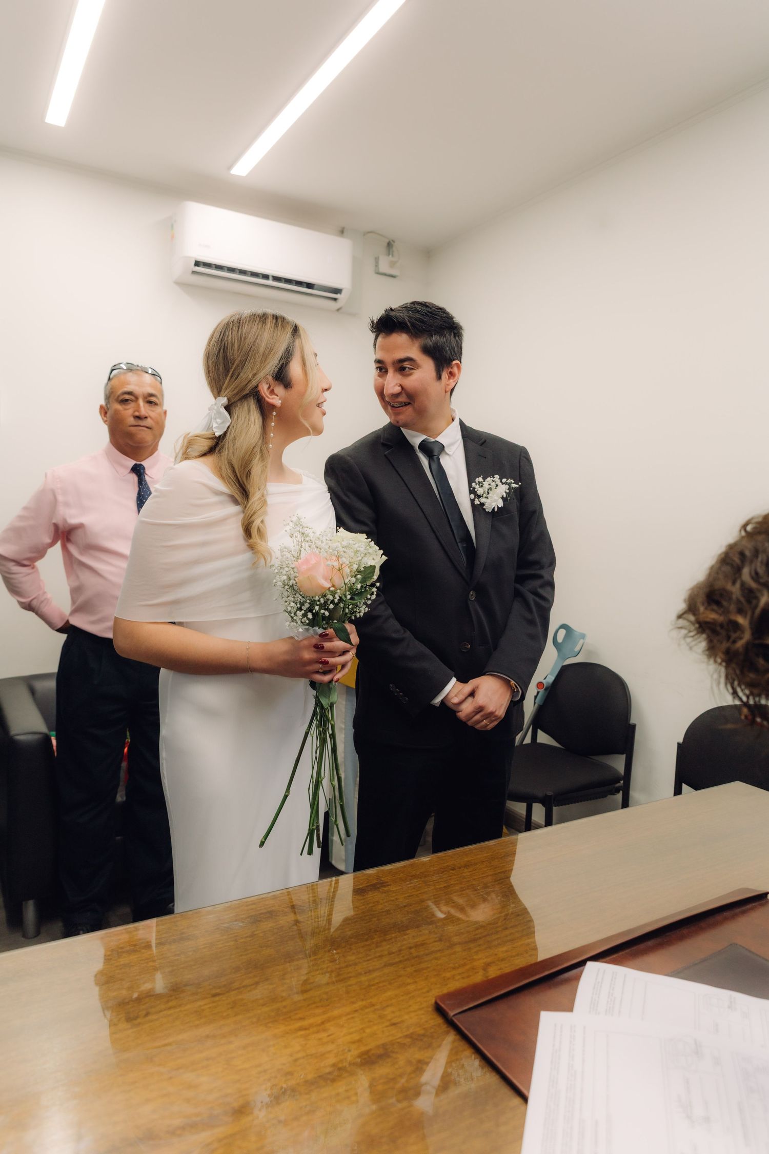 Bride and groom share a joyful moment at a civil wedding ceremony in a simple office setting.