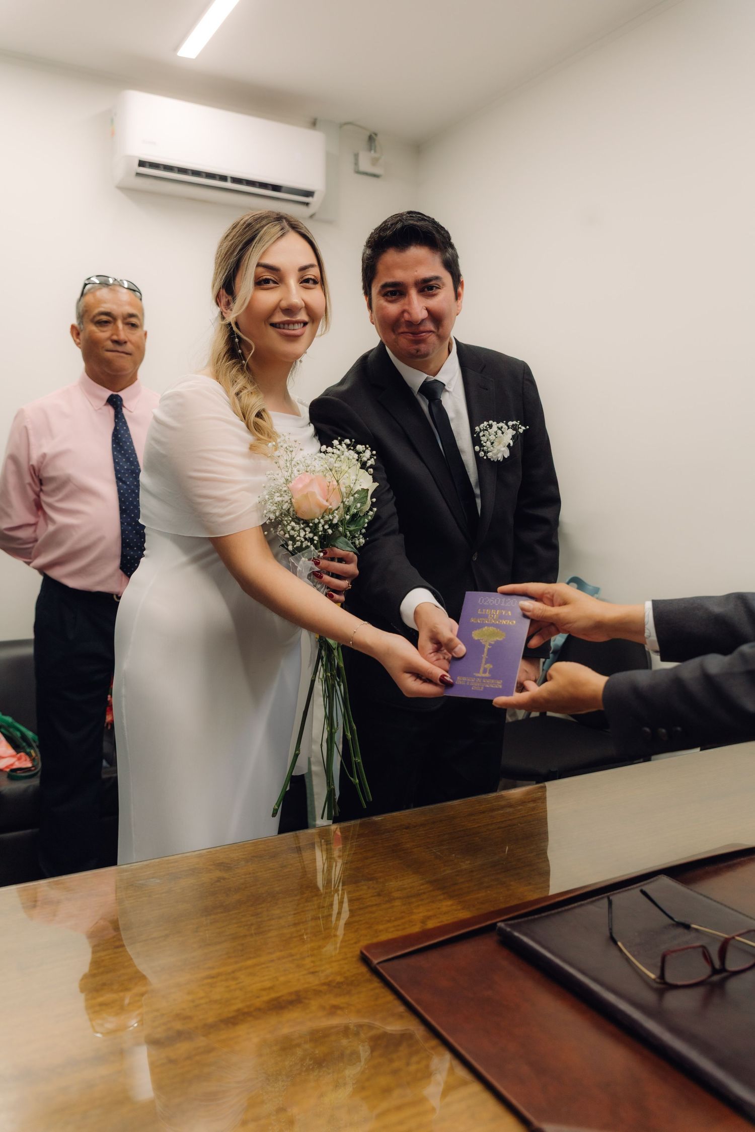 Bride and groom smiling while accepting purple marriage certificate from registrar at civil wedding ceremony.