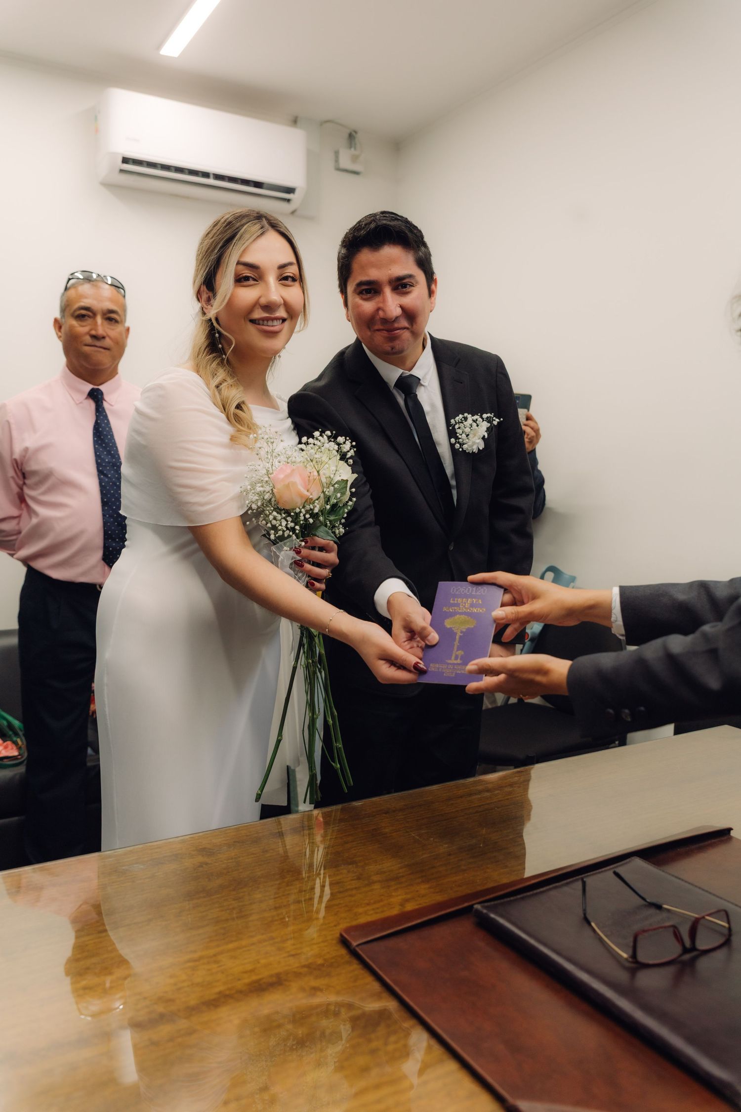 Happy newlyweds receiving their marriage certificate booklet from an official at a civil registry office.