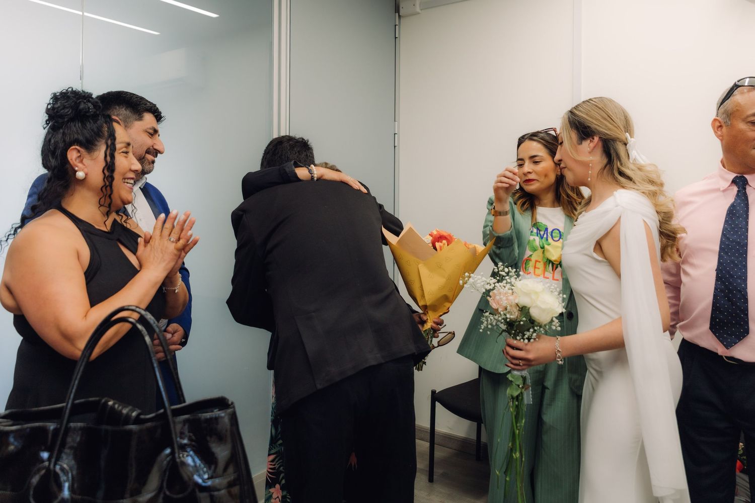 Wedding guests hugging and celebrating with the newlyweds after a civil ceremony indoors.