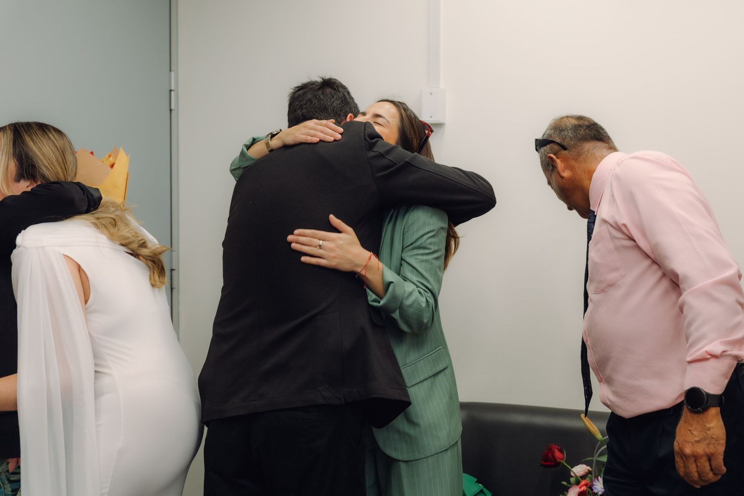 Groom embracing a woman in green suit while guests celebrate after civil wedding ceremony.