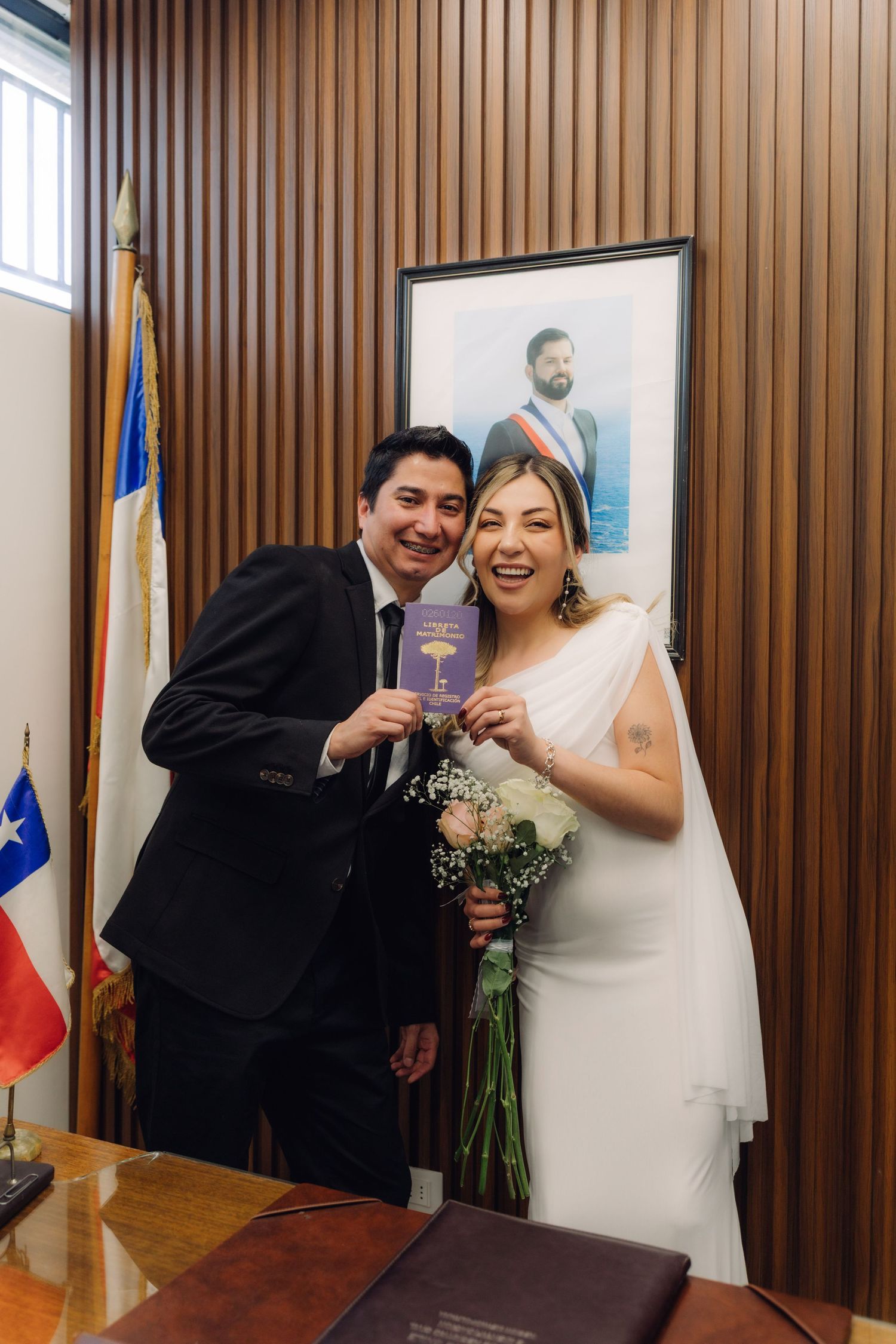 Newlyweds smiling and holding marriage certificate at Chilean civil wedding ceremony with Chilean flag.
