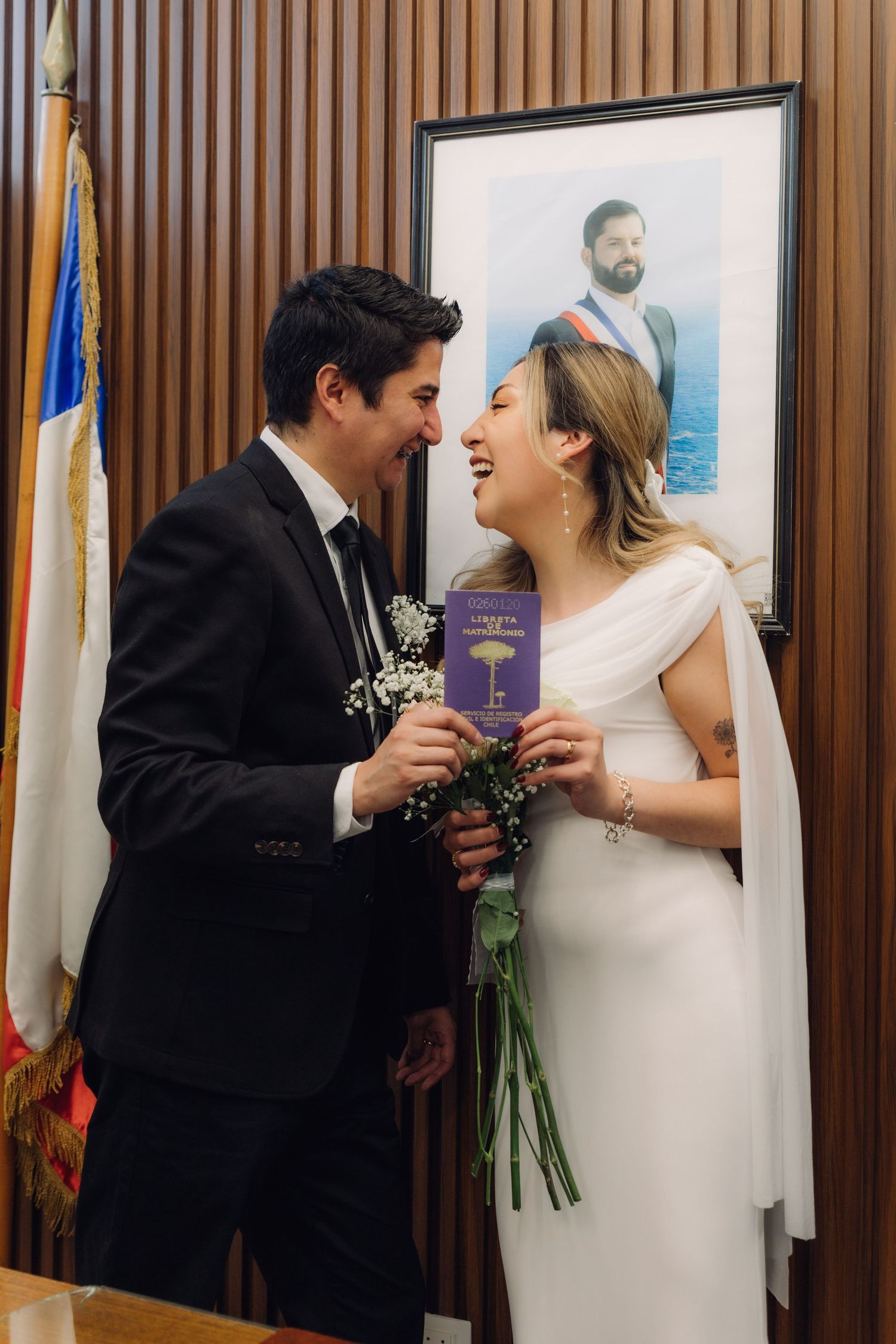 Happy newlyweds laughing together holding marriage certificate at Chilean civil wedding ceremony.