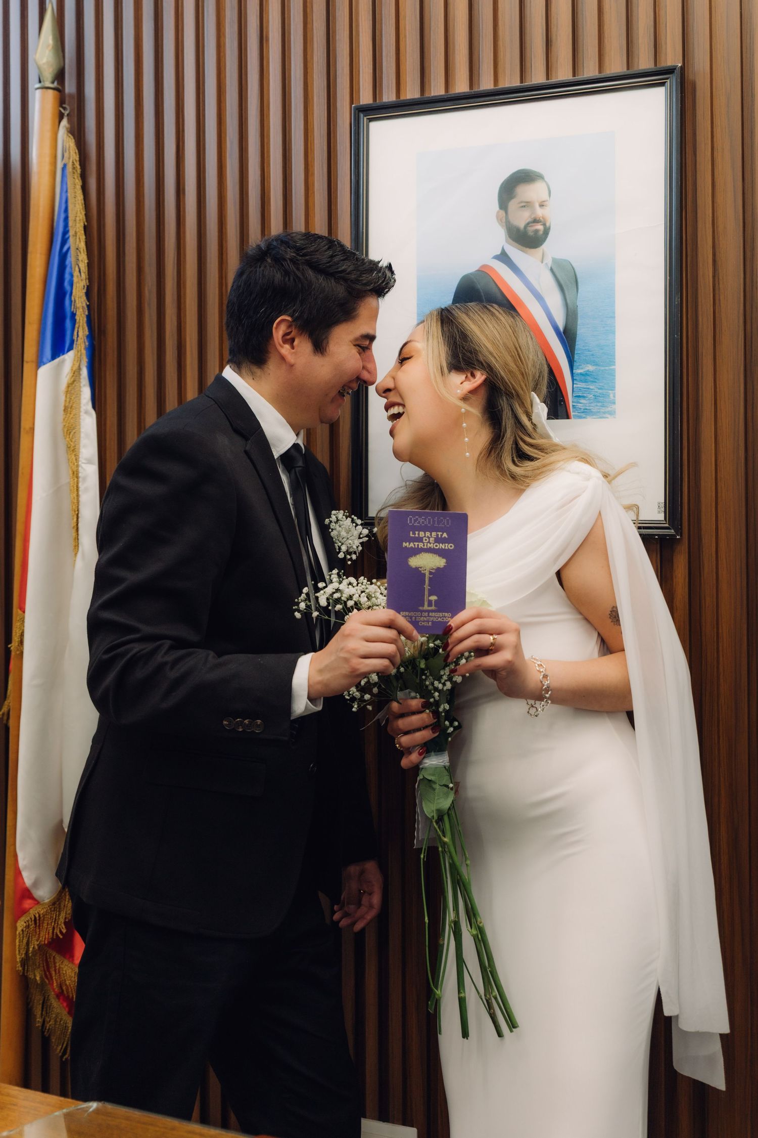 Joyful bride and groom sharing intimate moment with marriage booklet at Chilean civil ceremony.